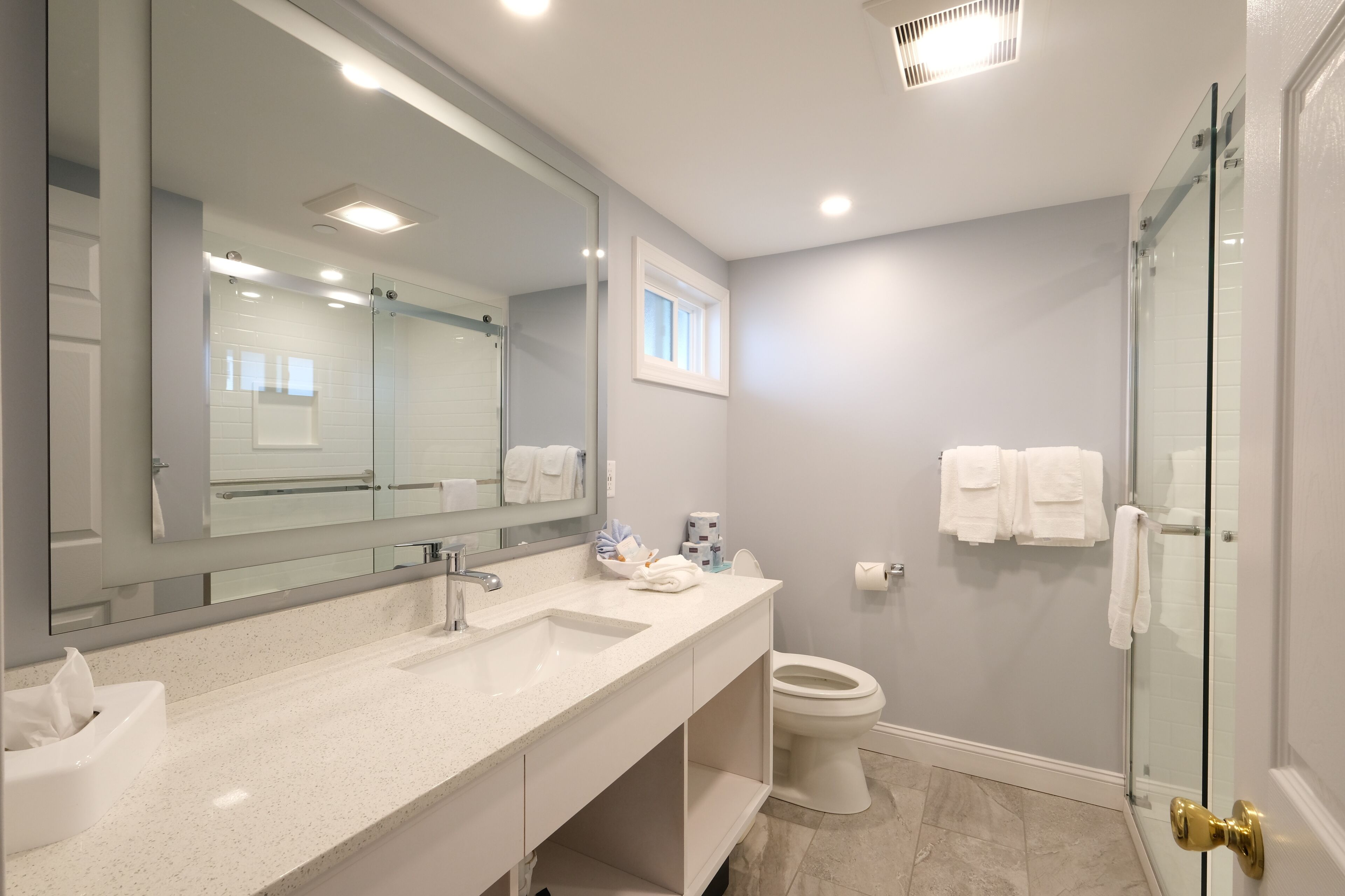 Un baño moderno con un espejo grande, un lavamanos, un inodoro y una cabina de ducha de vidrio.