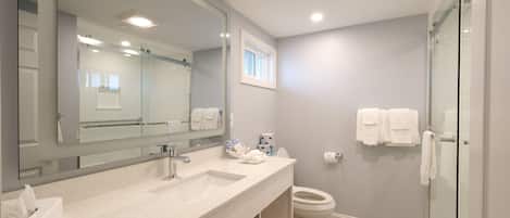 Un baño moderno con un espejo grande, un lavamanos, un inodoro y una cabina de ducha de vidrio.