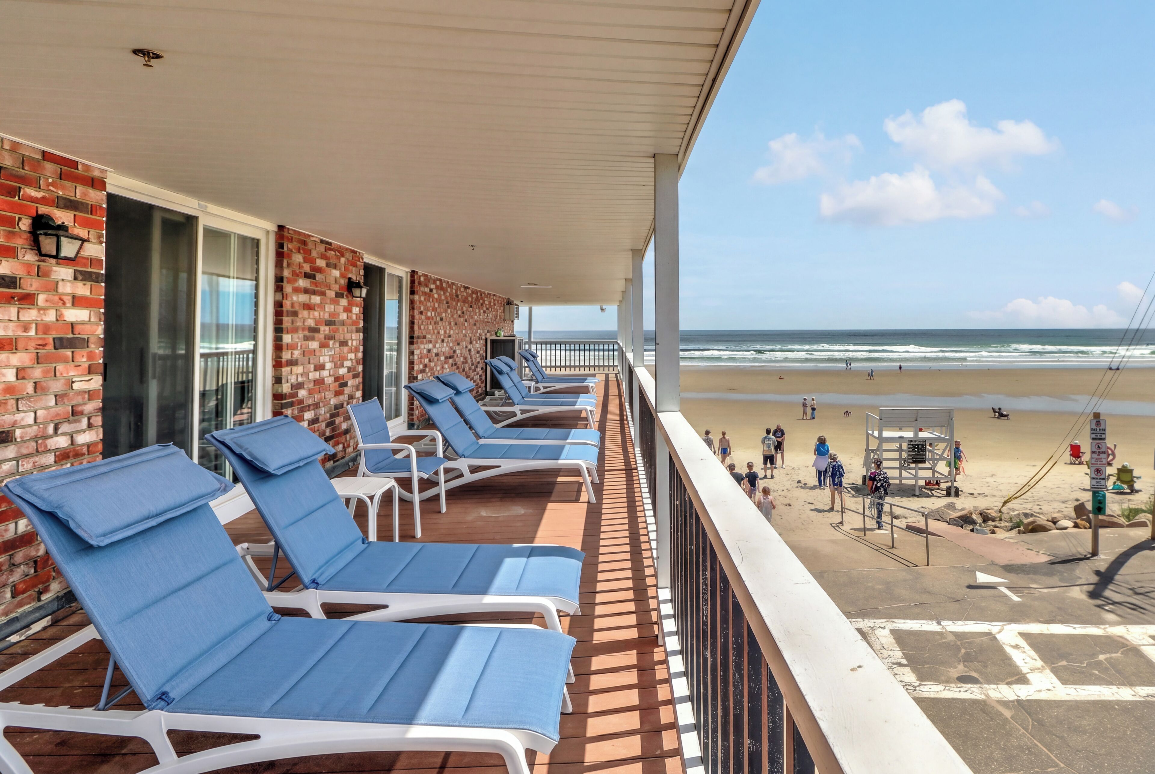 Ein Balkon mit blauen Liegestühlen, einer Backsteinmauer und Blick auf den Strand.
