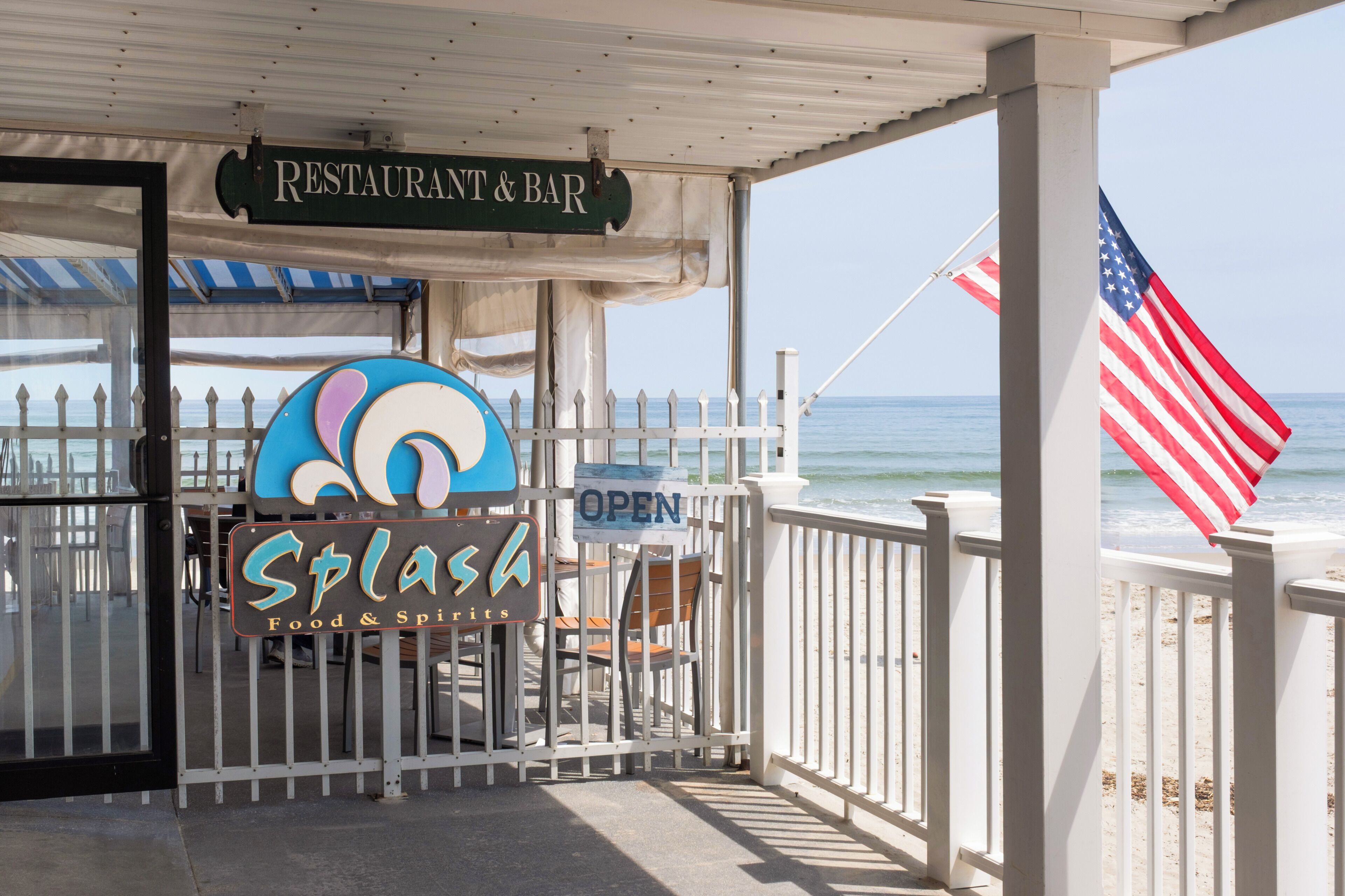 A beachside restaurant with an open sign, a flag, and a view of the ocean.