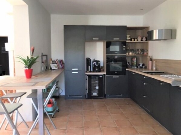 Uma cozinha moderna com armários cinza, micro-ondas, máquina de café e uma pequena área de jantar com mesa e cadeiras.