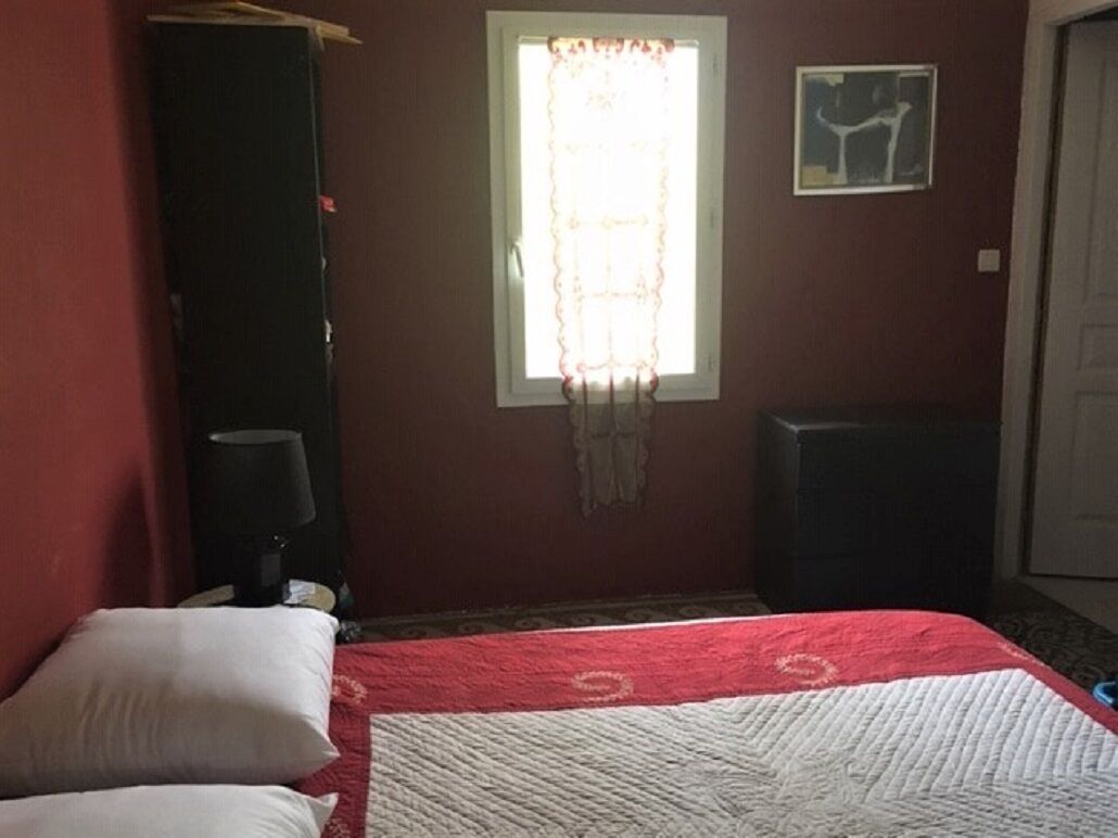A bedroom with a bed, a window with curtains, a wall-mounted artwork, and a door.