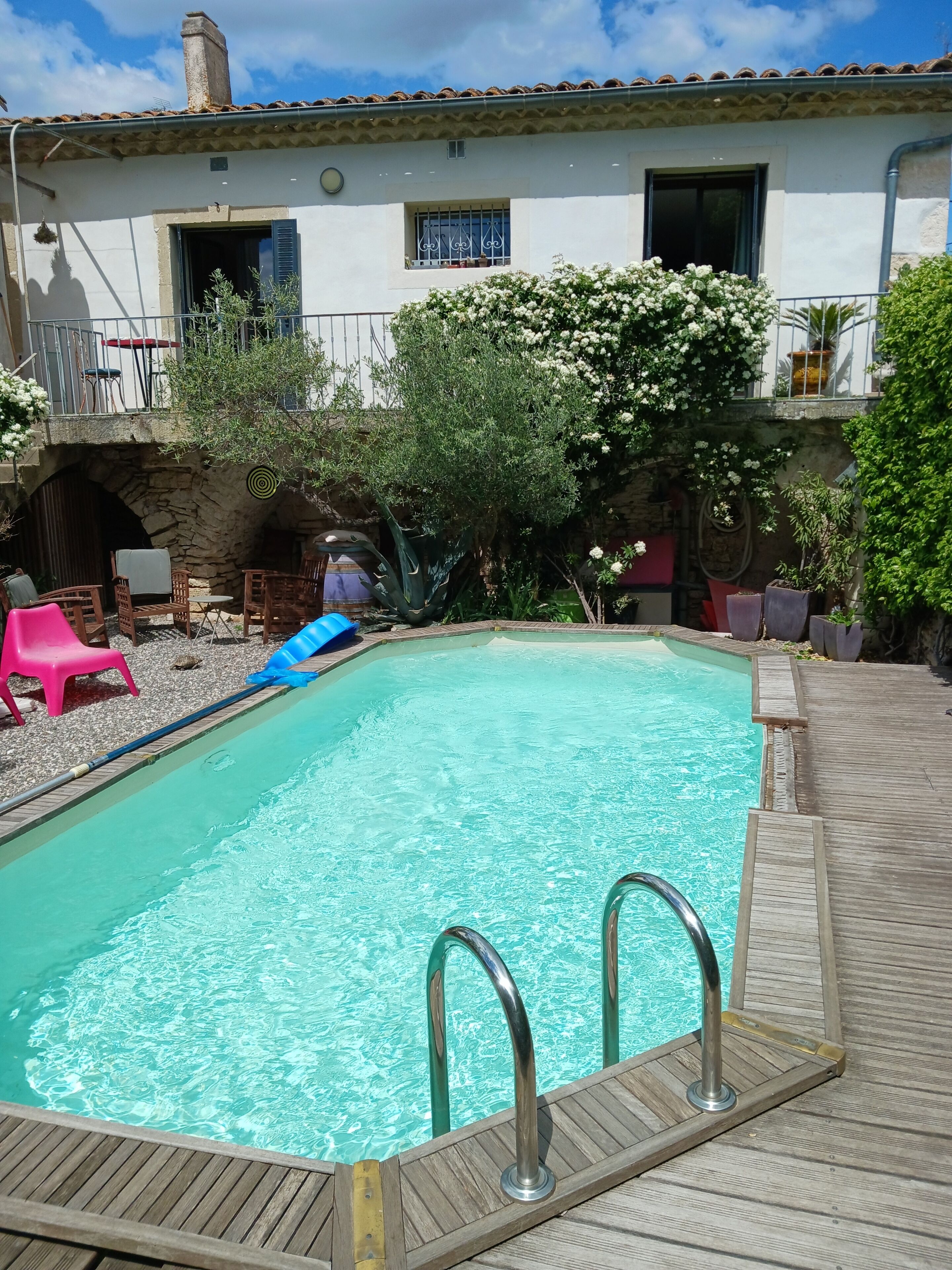 A swimming pool with a wooden deck, surrounded by outdoor furniture and plants.