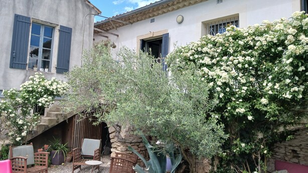 A courtyard with outdoor seating, a stone wall, and a building with blue shutters.