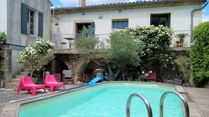 A swimming pool with a wooden deck, surrounded by potted plants and outdoor furniture.