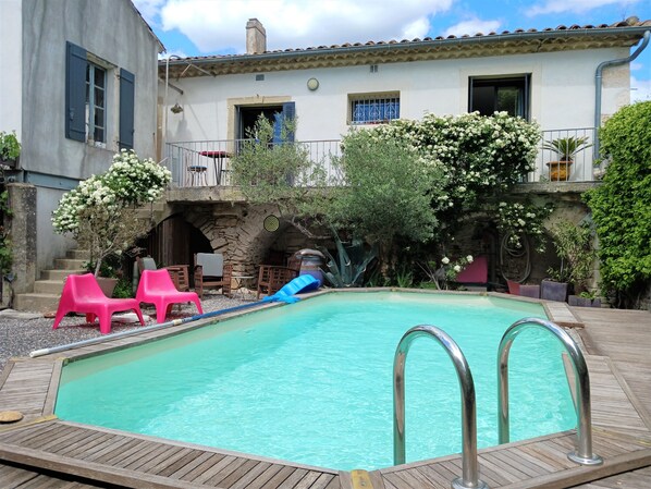 Una piscina con muelle de madera, rodeada de plantas en macetas y mobiliario de exterior.
