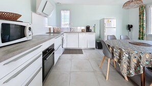 A compact kitchen with a microwave, sink, and refrigerator. There's a dining table with chairs and a patterned tablecloth. - Spacious cocoon in Narbonne - with sea view (Narbonne)