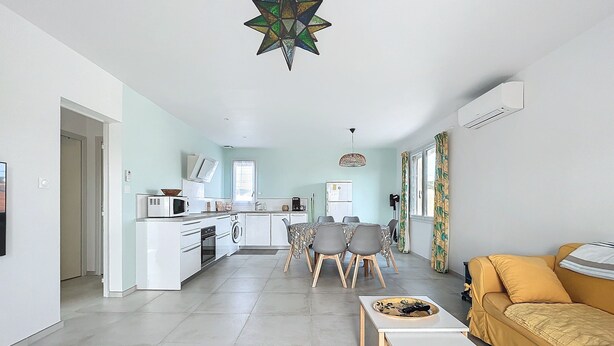 A modern kitchen with white cabinets, a microwave, and a washing machine. There is a dining area with a table and chairs, and a yellow sofa. - Spacious cocoon in Narbonne - with sea view (Narbonne)