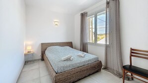 A bedroom with a bed, a nightstand, a lamp, a window with curtains, and a chair. - Spacious cocoon in Narbonne - with sea view (Narbonne)
