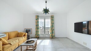 A living room with a sofa, a coffee table, a TV mounted on the wall, and a door leading outside. - Spacious cocoon in Narbonne - with sea view (Narbonne)