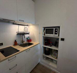 A compact kitchen with a sink, a black induction cooktop, a microwave, and a small shelf with a coffee maker and a framed picture. - Bright cocoon in Sainte-Maxime - close to the sea (Sainte-Maxime)
