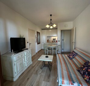 A compact living space with a television, a dining table, a kitchen area, and a bed.