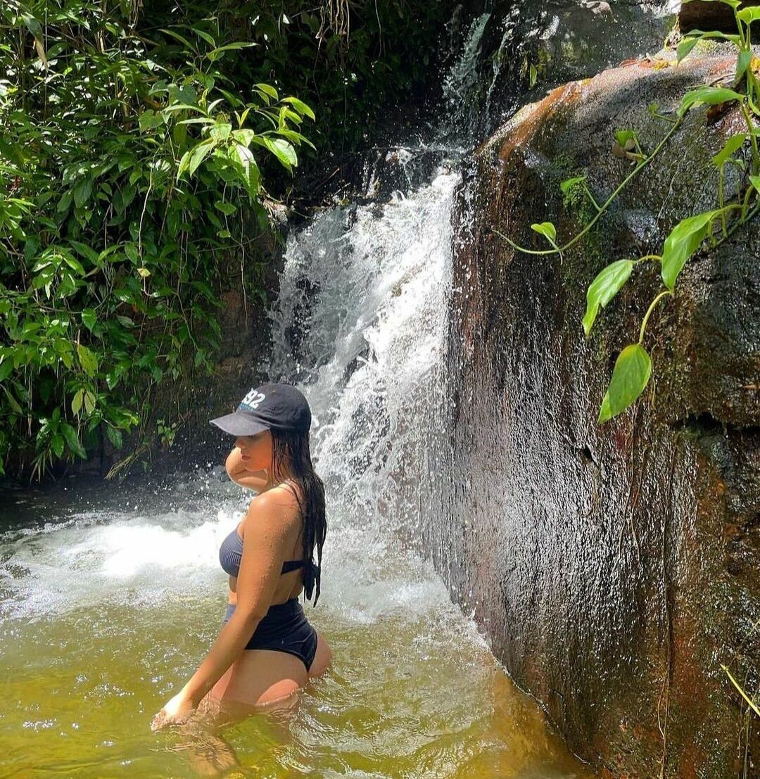 A person sitting in a natural water setting with a waterfall in the background.