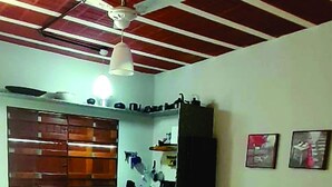 A bedroom with a bed, a desk, a chair, a ceiling fan, and a window.