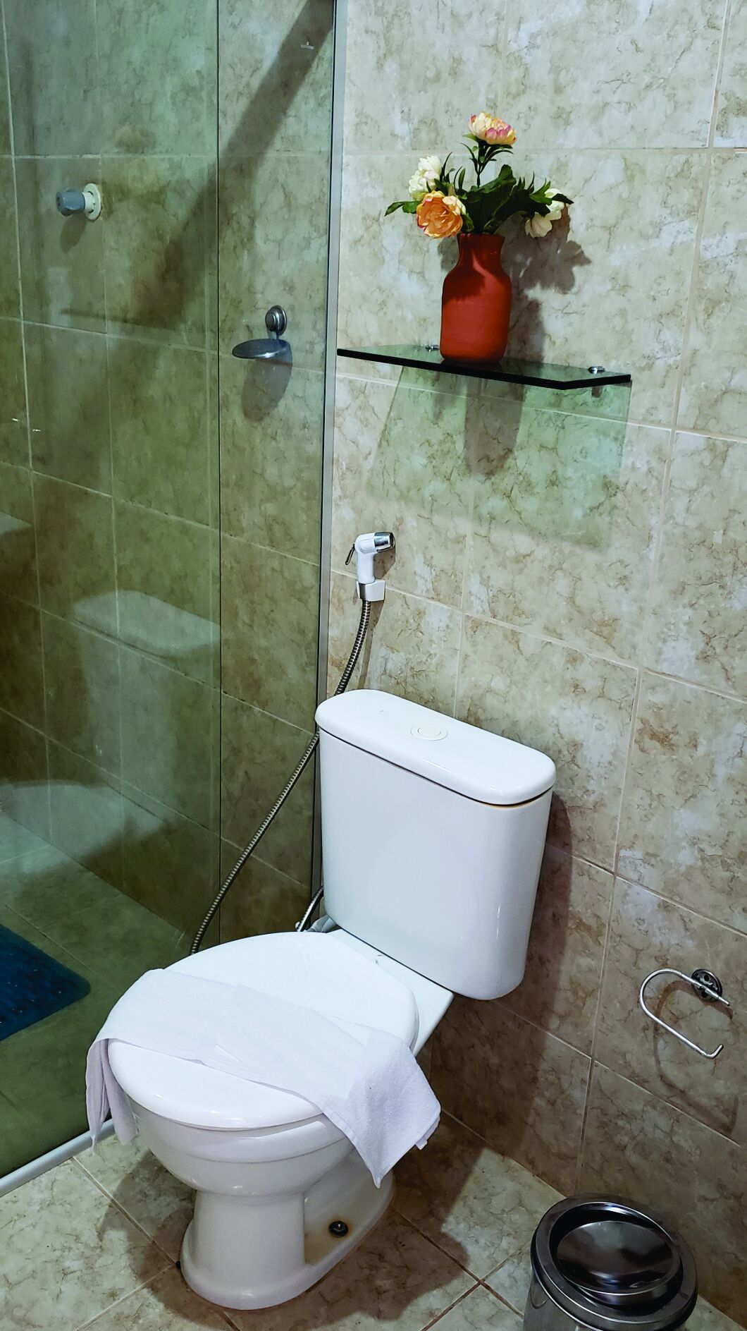 A bathroom with a toilet, a glass shower enclosure, and a shelf with a vase of flowers.