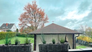 A gazebo with a tiled roof, surrounded by potted plants, and a string of lights above. - Cozy vacation apartment for 4 people (Baumholder)