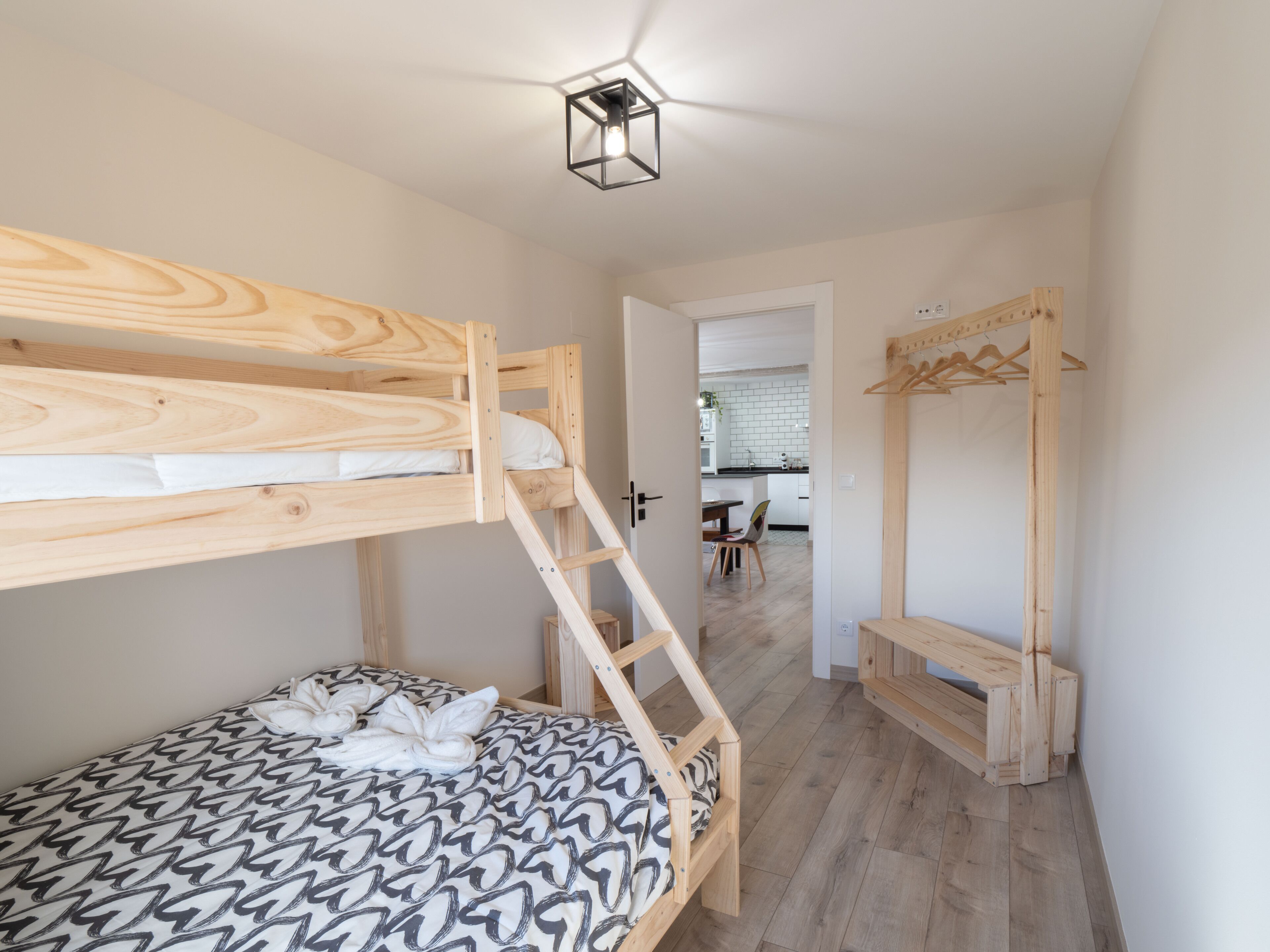 Une chambre avec un lit superposé, une échelle en bois, une couvre-lit à motifs et un portant à vêtements suspendu.