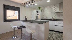 A modern kitchen with a central island, white cabinetry, a built-in oven, and a window overlooking a brick wall. - The Moradel Moncayo  (Añón de Moncayo)