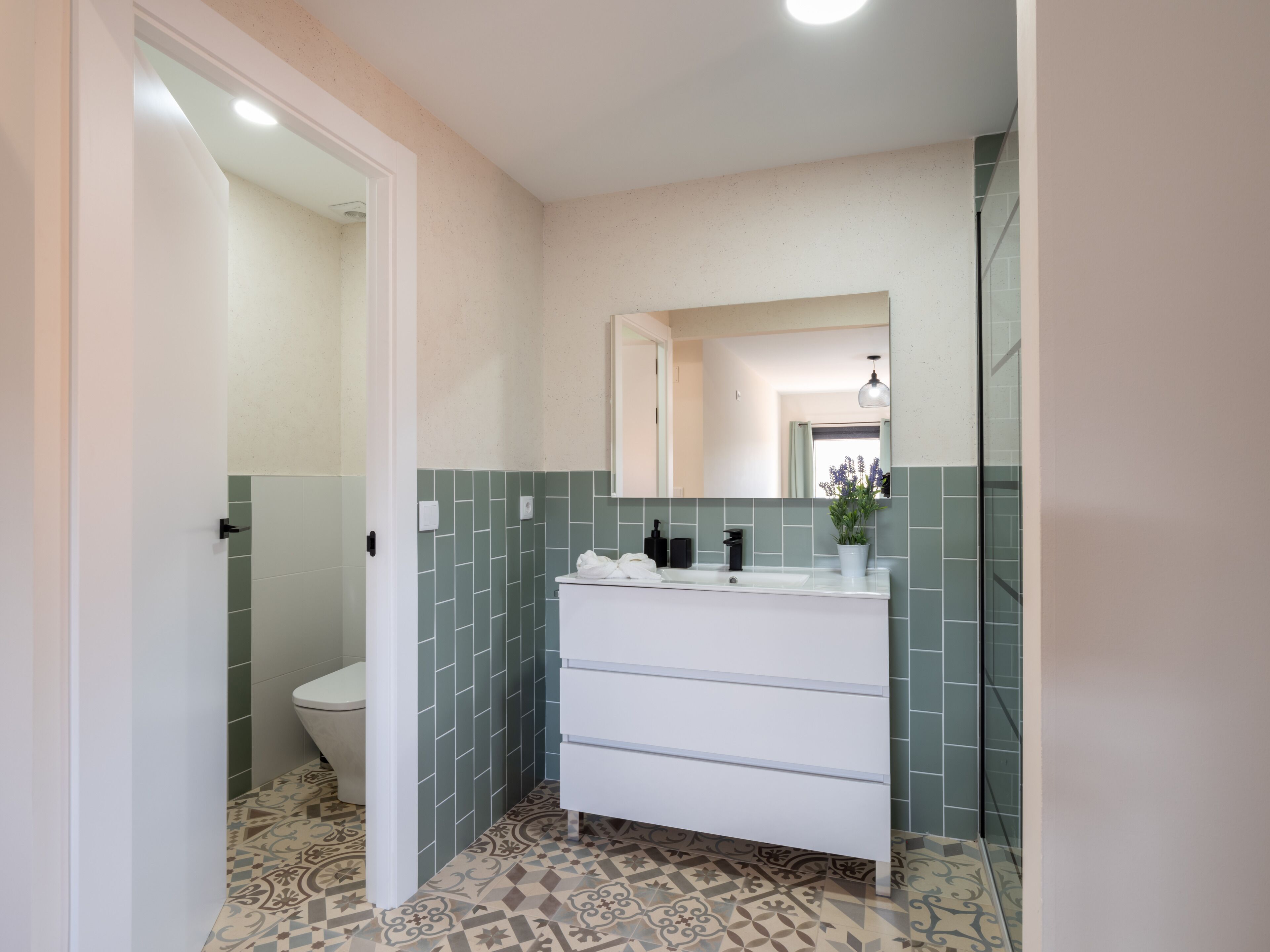 Un baño con lavamanos blanco, azulejos verdes y baldosas de suelo con diseño.