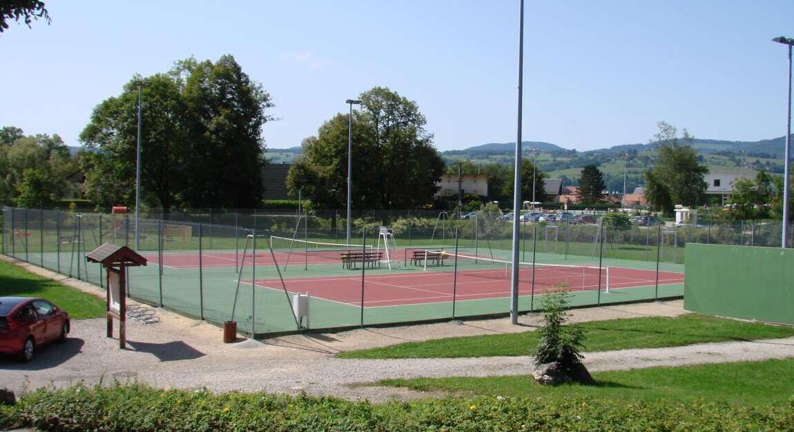A tennis court with a fence, a small pavilion, and a car parked nearby.