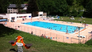 A swimming pool surrounded by a fenced area with a grassy hill in the background. - Le charmant Songe en Chartreuse (Saint-Pierre-de-Chartreuse)