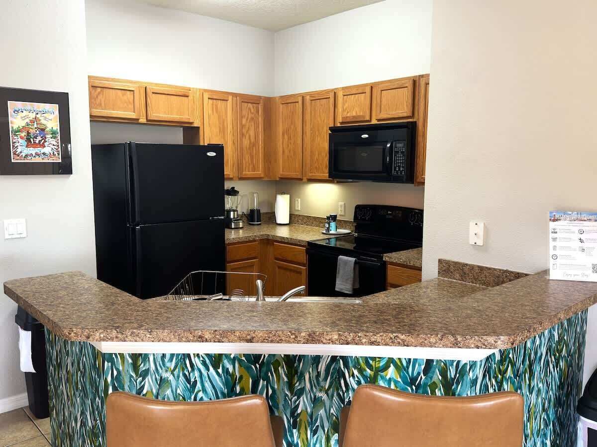 A kitchen with wooden cabinets, a black refrigerator, a microwave, and a granite countertop.