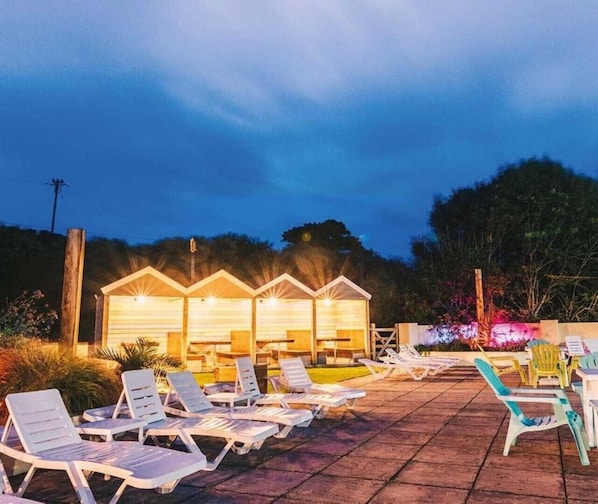 A patio area with lounge chairs and wooden cabins with lights.