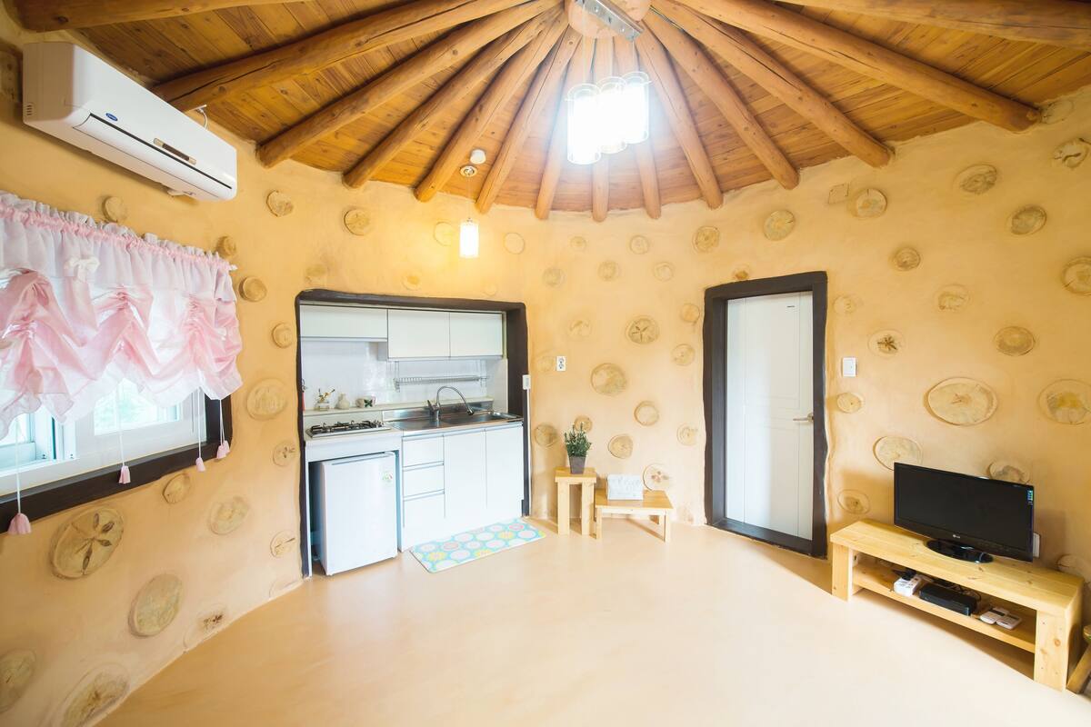 A compact room with a kitchenette, a television on a wooden stand, and a ceiling with wooden beams.