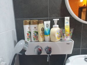 A bathroom shelf with various toiletries including a bottle of lotion, a bottle of shampoo, and a tube of toothpaste. - Red Clay Pension (Gangneung)