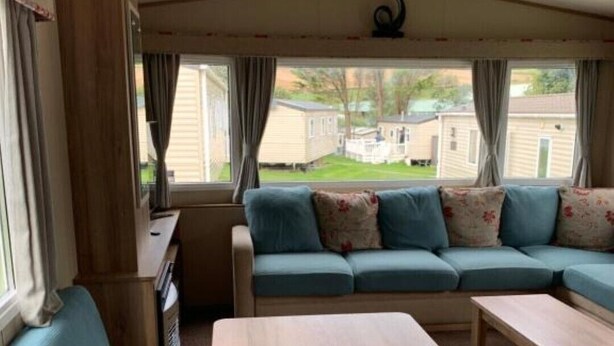 Interior acogedor de una autocaravana con un sofá, una mesa de madera y una ventana que da a un barrio residencial.
