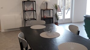 En matplats med ett mörkt träbord, vita bordsunderlägg och svarta stolar. Det finns två svarta hyllor med dekorativa föremål och en krukväxt.