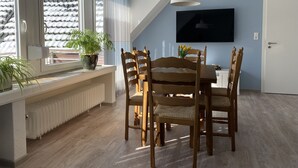 A dining area with a table and chairs, a potted plant, a radiator, and a television on the wall. - Generously equipped and very spacious, family vacation apartment (4) (Lembruch)