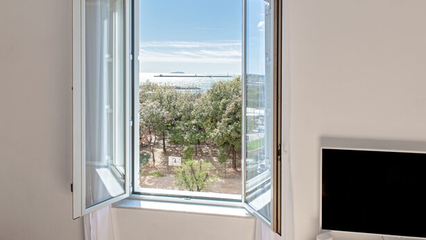 A room with a large open window, a flat-screen TV, and a white wall.