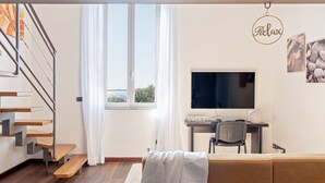 A modern living room with a staircase, a flat-screen TV, a desk, and a couch.