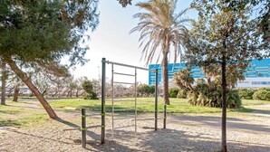 An outdoor gym area with exercise equipment, surrounded by trees and a building in the background.