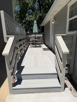 Una terraza de madera con barandilla, una mesa con sillas y una sombrilla.