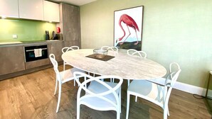 Eine moderne Küche mit weißen Schränken, einem runden Esstisch mit weißen Stühlen und einem großen Flamingo-Gemälde an der Wand.