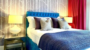 Ein Hotelzimmer mit einem großen Bett, einem Nachttisch mit Lampe, einem roten Vorhang und einer Wand mit Baummuster.
