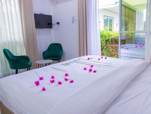A hotel room with a bed, two green chairs, a small table, and a TV mounted on the wall. - Nihaali Maldives (Kudarikilu)