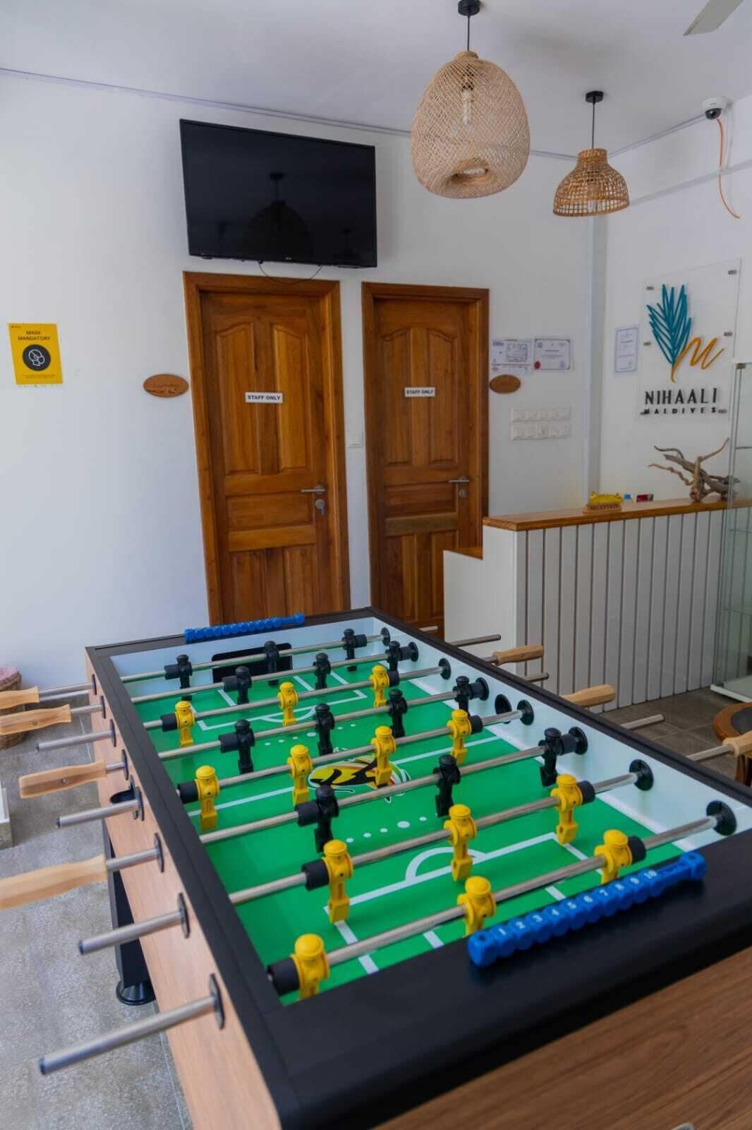 Una habitación con mesa de fútbol de mesa, dos puertas de madera, un televisor y un letrero que indica acceso 'solo para empleados'.