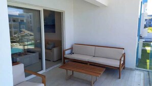 Un balcón con un sofá, una mesa de madera y un ventanal de vidrio que da a una zona de piscina.
