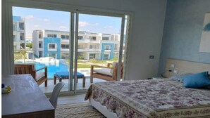 Habitación de hotel con cama, una mesa y una silla. Posee un ventanal corredero que da a una zona de piscina.