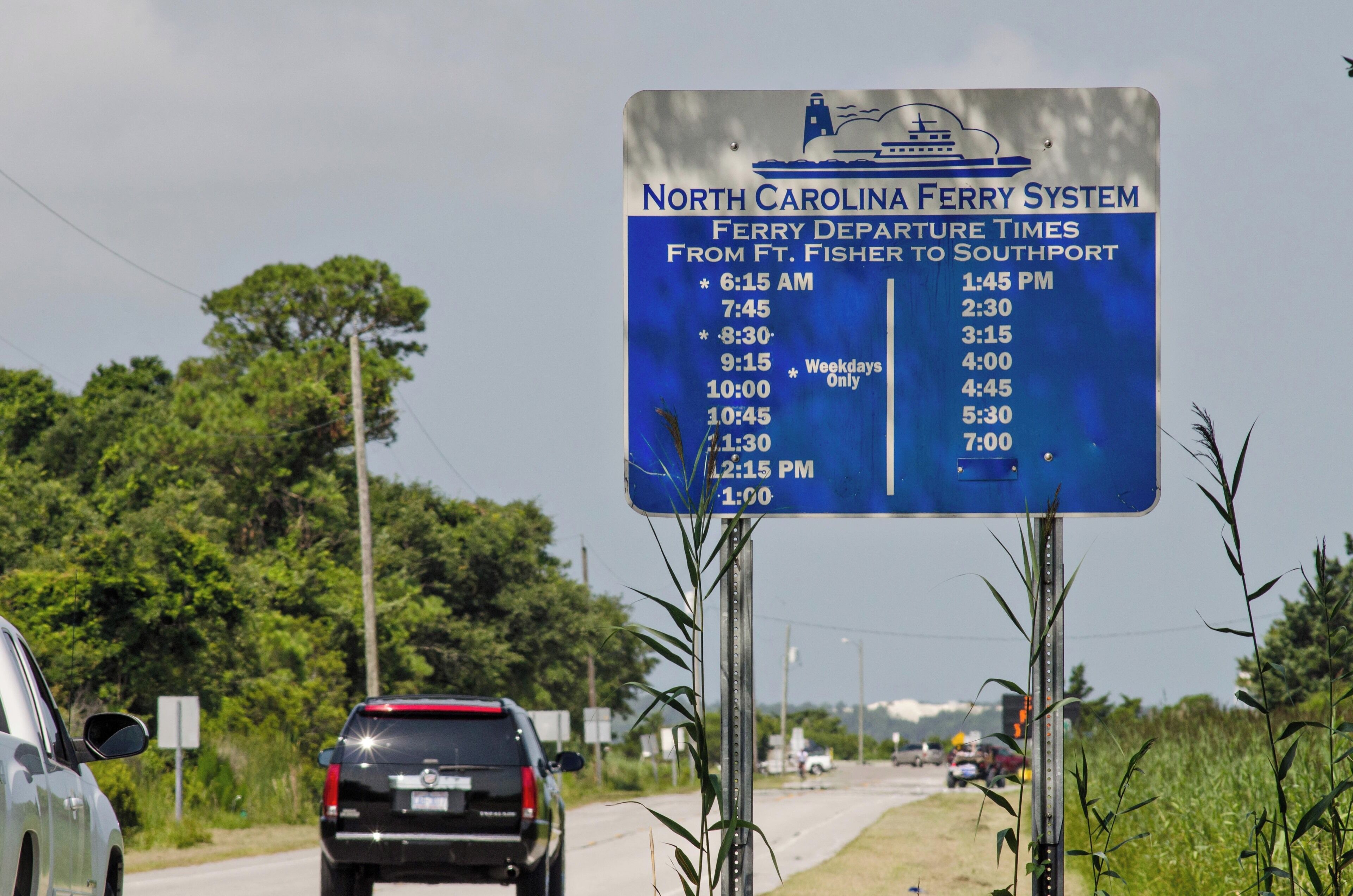 A blue sign with ferry departure times for North Carolina Ferry System from Ft. Fisher to Southport.