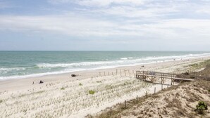 A beach with a wooden boardwalk leading to the shore, sandy dunes, and the ocean. - Spacious ocean front condo in Ocean Dunes! (Kure Beach)