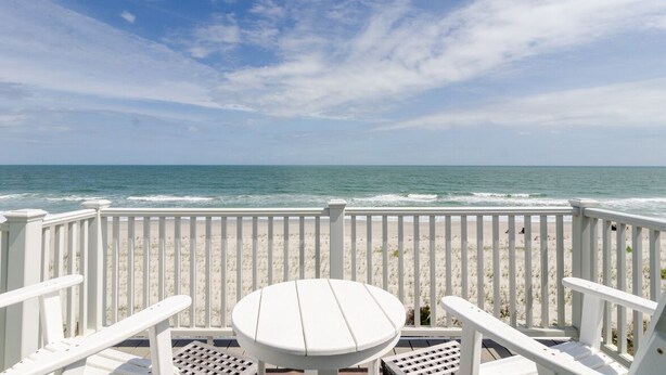 A beach view from a balcony with white railings and a round table. - Spacious ocean front condo in Ocean Dunes! (Kure Beach)