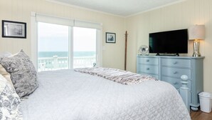 A bedroom with a bed, a dresser, a television, and a window with a view of the ocean. - Spacious ocean front condo in Ocean Dunes! (Kure Beach)