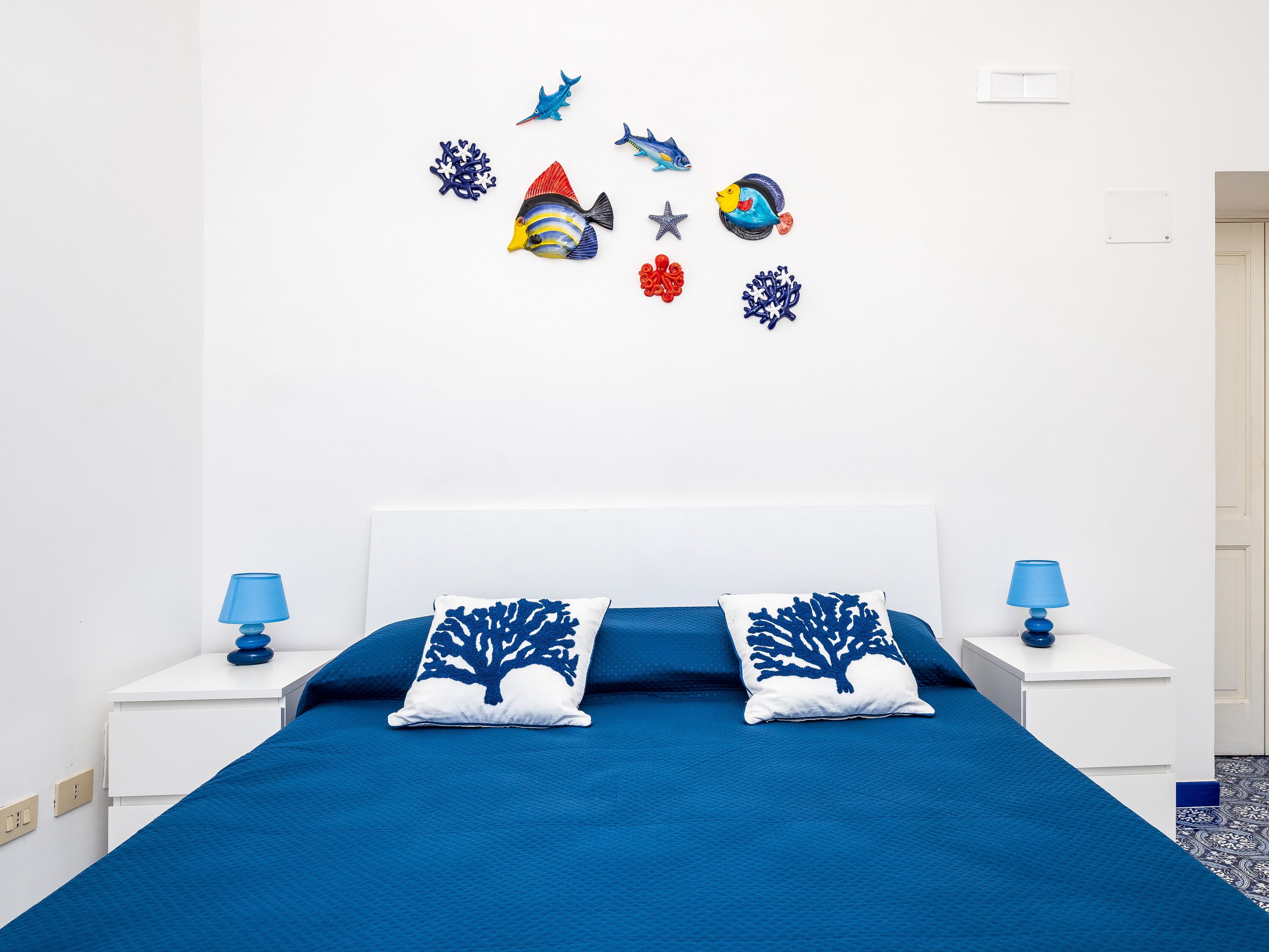 A bedroom with a blue bedspread, two matching pillows, a white headboard, and a wall decorated with marine-themed wall stickers.