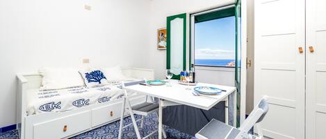 Une pièce avec un lit, une table et une chaise, une fenêtre donnant sur un paysage agréable et une porte.