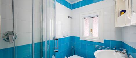 A bathroom with a glass shower enclosure, a toilet, and a sink.