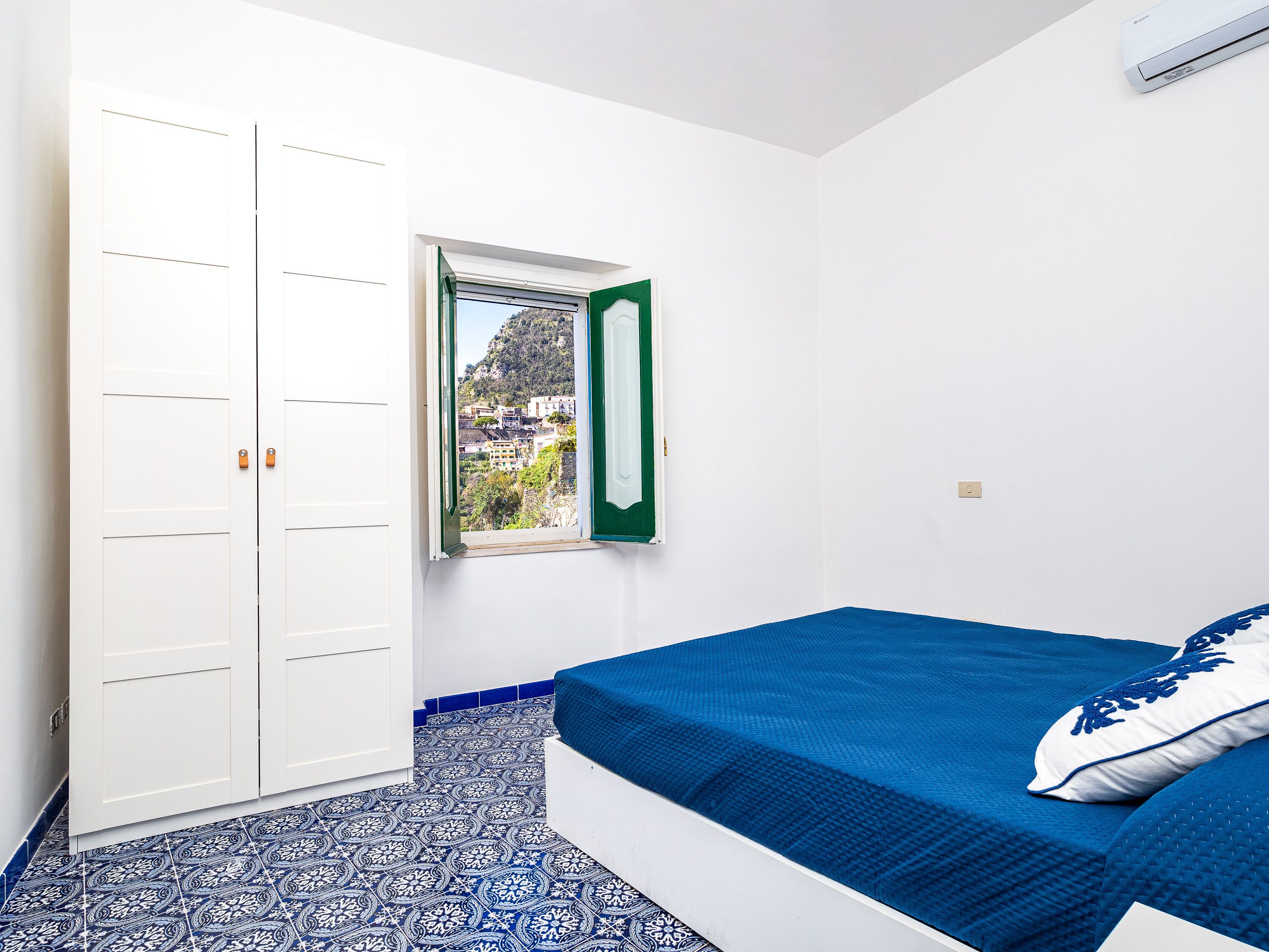 Una camera da letto con un letto, un armadio, una finestra vista edifici e piastrelle a pavimento decorate.